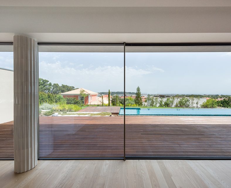 A sleek large scale window frame looks out onto a backyard and the ocean beyond.